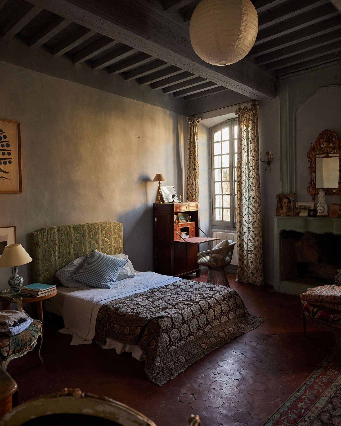 Bedroom interior featuring a bed with patterned textiles, a desk by the window, and soft, diffused lighting creating a warm atmosphere.