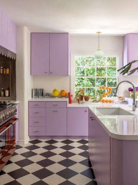 A modern kitchen featuring lilac cabinets, a black and white checkered floor, and fresh oranges arranged near a window.