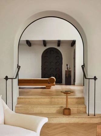 Indoor view showcasing a tan daybed, decorative table and sculpture, dark wood door, and a cream-colored couch within a home setting.