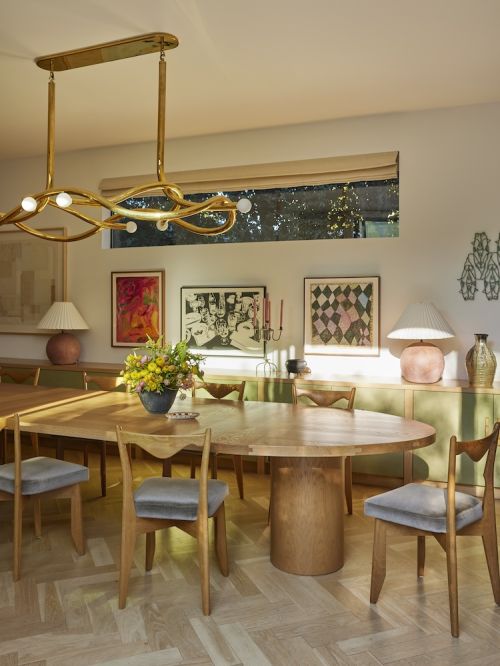 Dining room interior featuring a wooden table with chairs, a floral arrangement, artwork, and a unique gold chandelier.