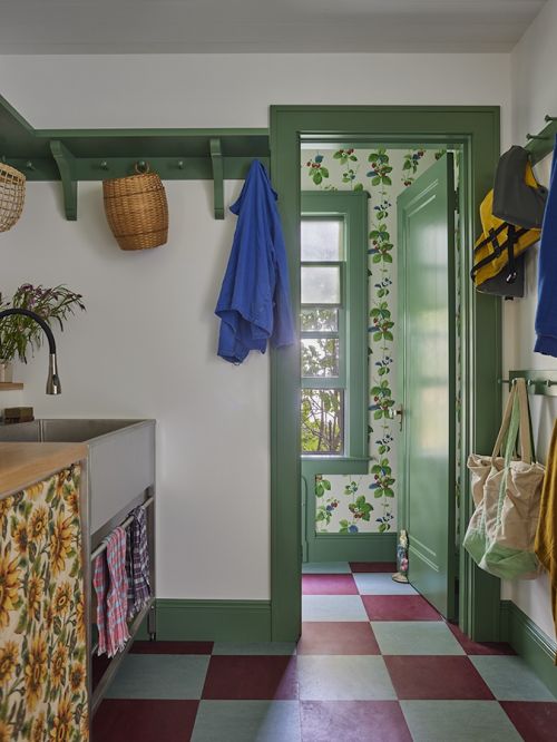 An interior view of a mudroom with green trim, a stainless steel sink, colorful accents, and a doorway leading to another room.