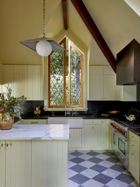 Bright kitchen with island and stainless-steel range oven. Diamond checkered floor, marble countertops, and paneled cabinets.