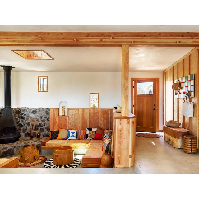 Interior of a living room featuring a stone fireplace, wood-paneled walls, built-in seating with colorful pillows, and unique wooden stools.