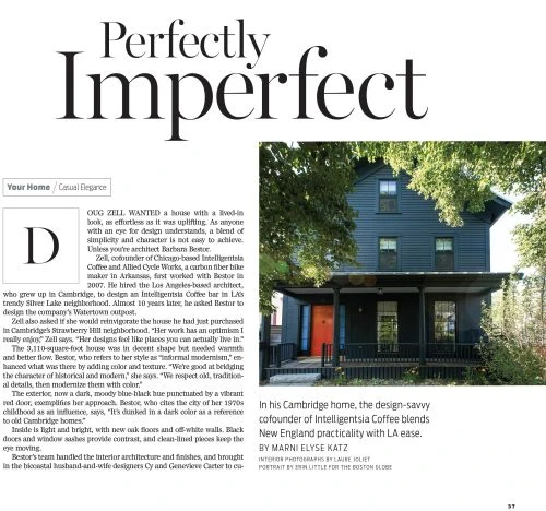 Three-story dark blue house with a vibrant red front door, green trees overhead, and small front porch.