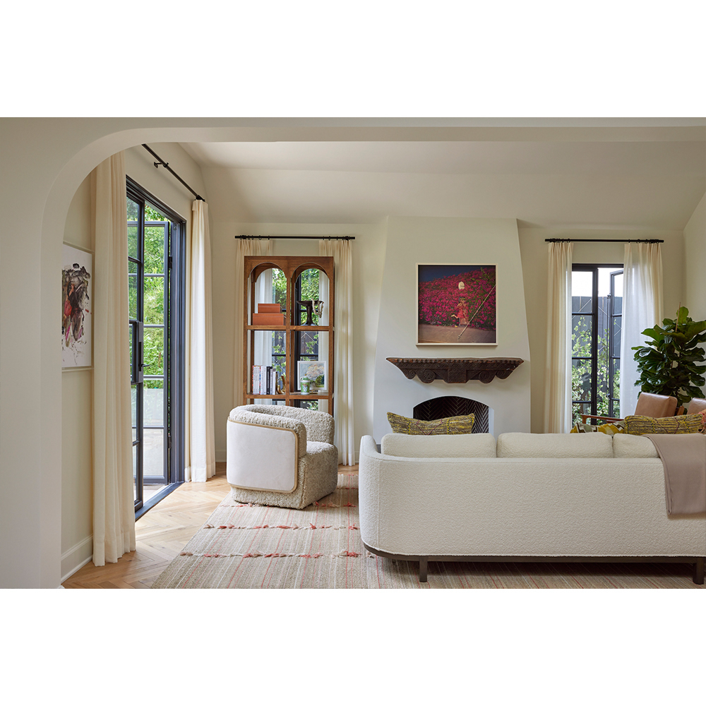 Modern living room interior with cream boucle sofa, curved armchair, fireplace, and arched glass doors by Laure Joliet.