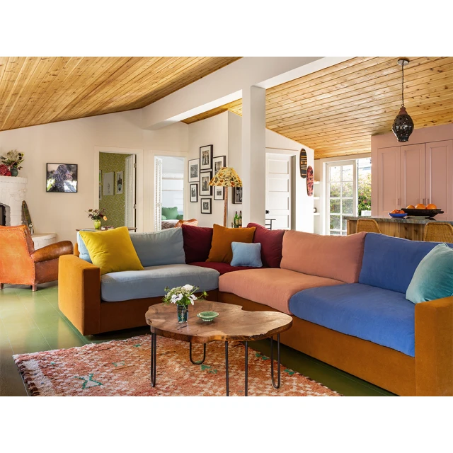 Living room interior with a colorful sectional sofa, wooden coffee table, patterned rug, and light wood ceiling, creating a cozy atmosphere.