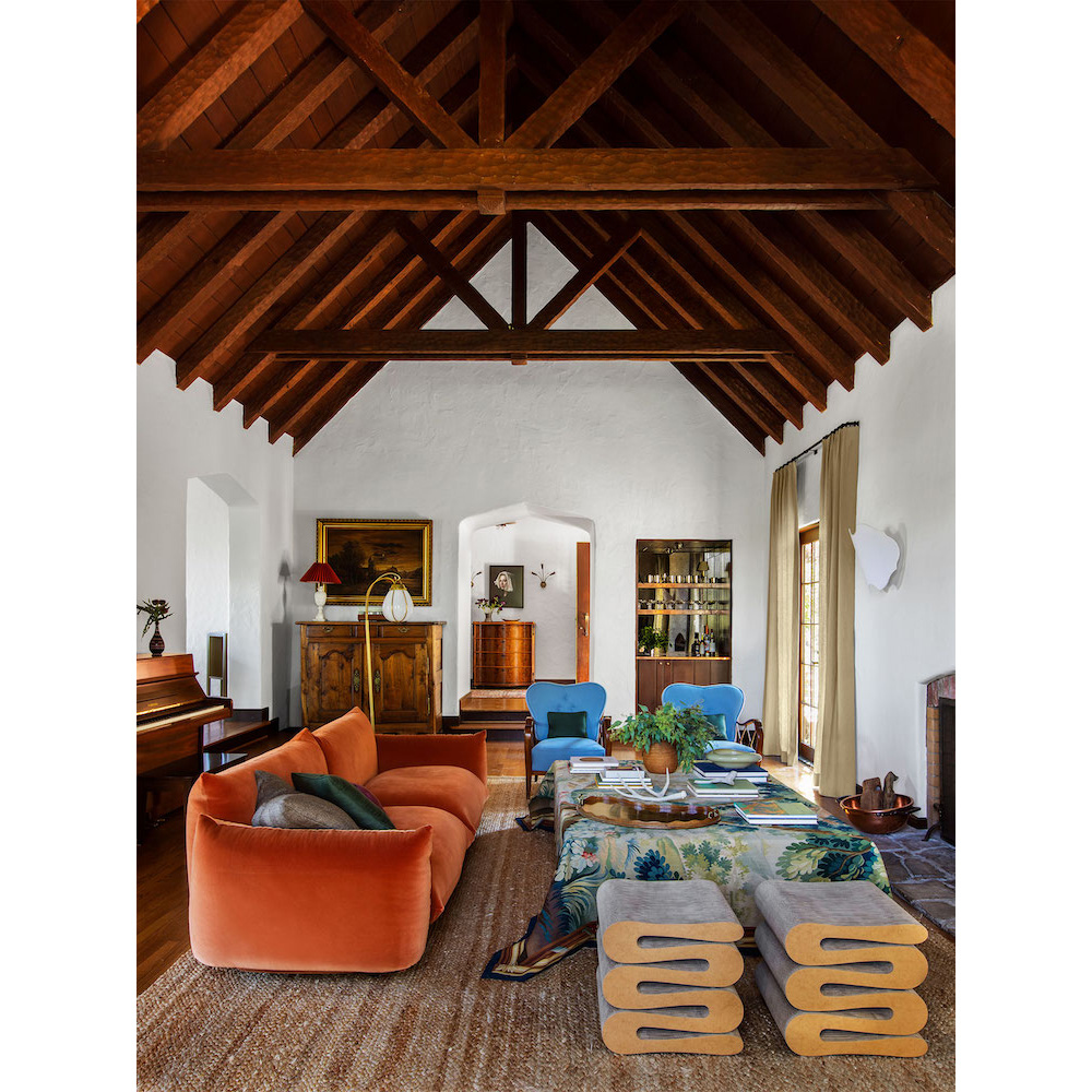 Eclectic living room interior with orange velvet sofa, patterned rug, wood ceiling beams, and stylish furniture arrangement.