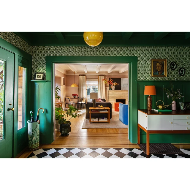 Interior view of a home hallway leading to a living area, featuring green walls, patterned wallpaper, and a black-and-white checkered floor.