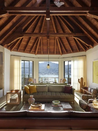 Living room interior with a large sofa, wooden coffee table, floor lamp, and a view of a lake and mountains through large windows.