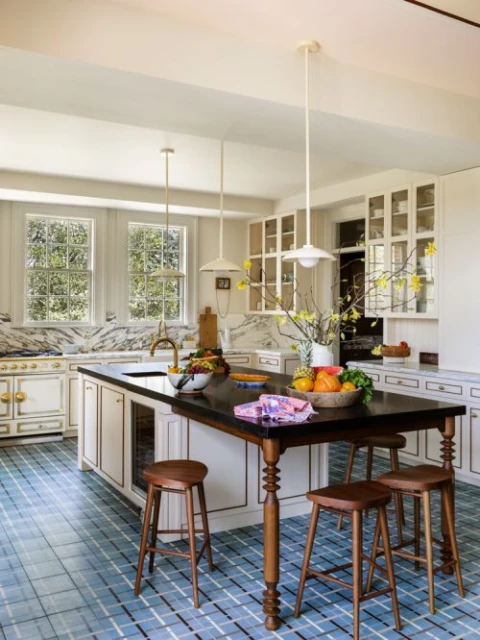 Bright and airy kitchen with an island, fruit, stools, and pendant lights against white cabinetry and a tiled floor.
