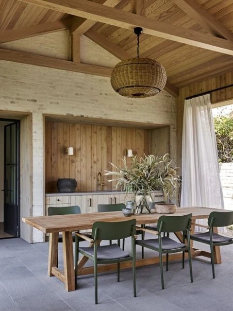 Indoor dining space featuring a wooden table surrounded by green chairs, a wicker pendant light, and a wooden wall with decor.