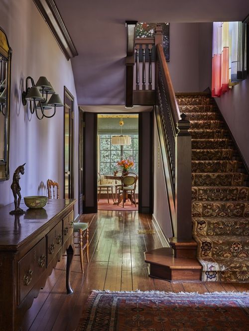Interior view of a home hallway featuring a wood staircase, wooden furniture, and natural light, creating a warm and inviting atmosphere.