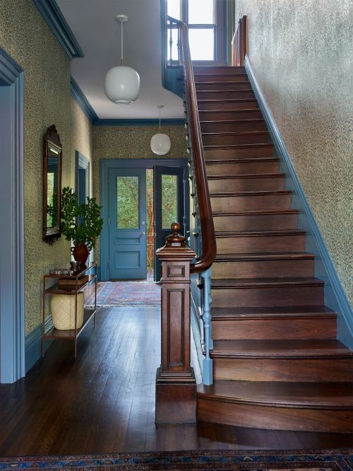 An interior shot showcases a staircase with rich wood tones, complemented by blue-trimmed doorways and walls with patterned wallpaper.