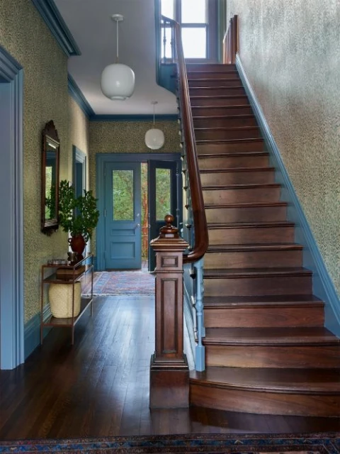 An interior shot showcases a staircase with rich wood tones, complemented by blue-trimmed doorways and walls with patterned wallpaper.