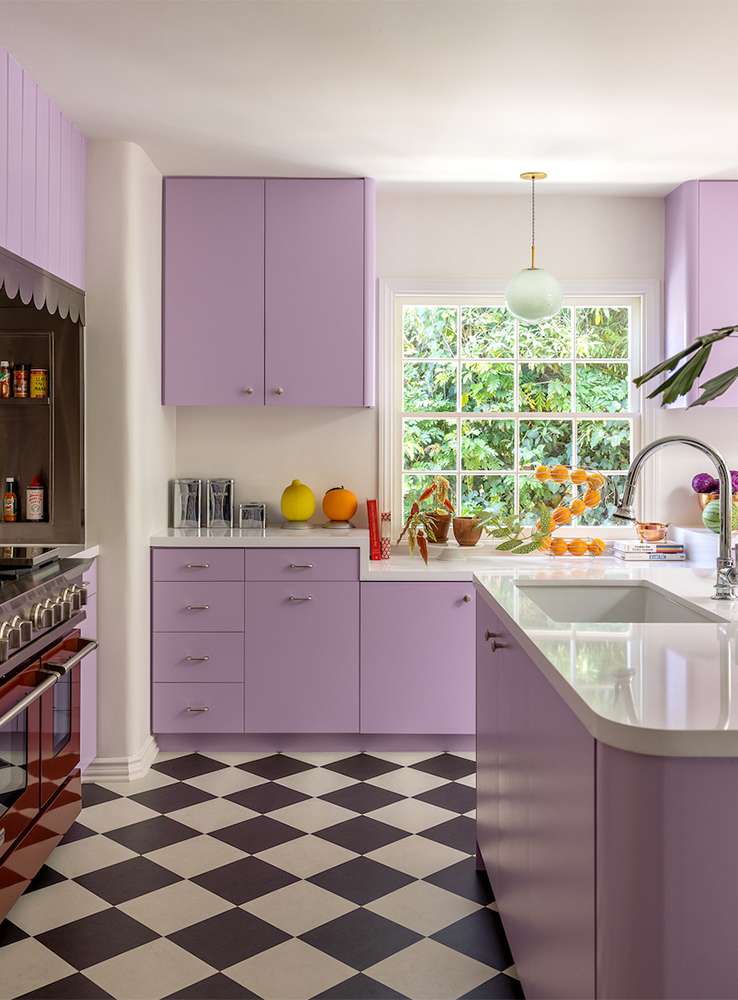 Bright kitchen features lilac cabinetry, white countertops, and a black and white checkerboard floor; natural light from window.