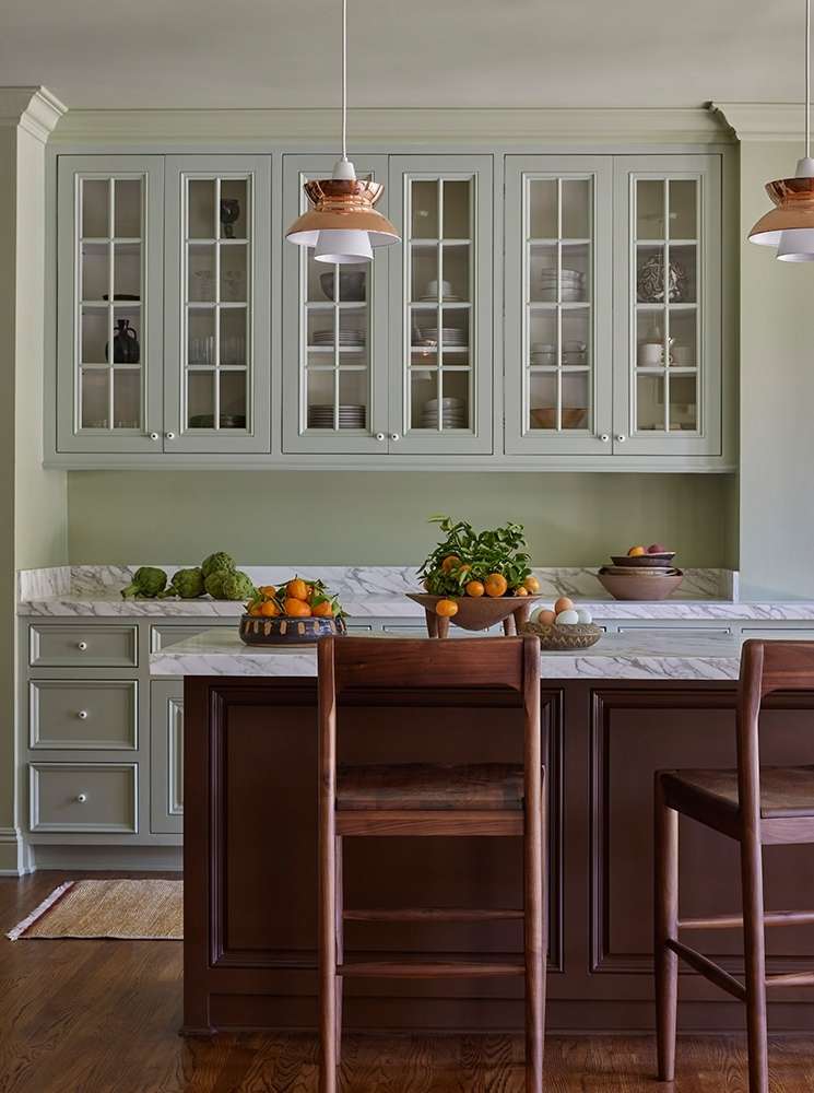 Interior kitchen view featuring mint-green cabinets, brown wooden kitchen island with stools, marble countertop, and pendant lights.