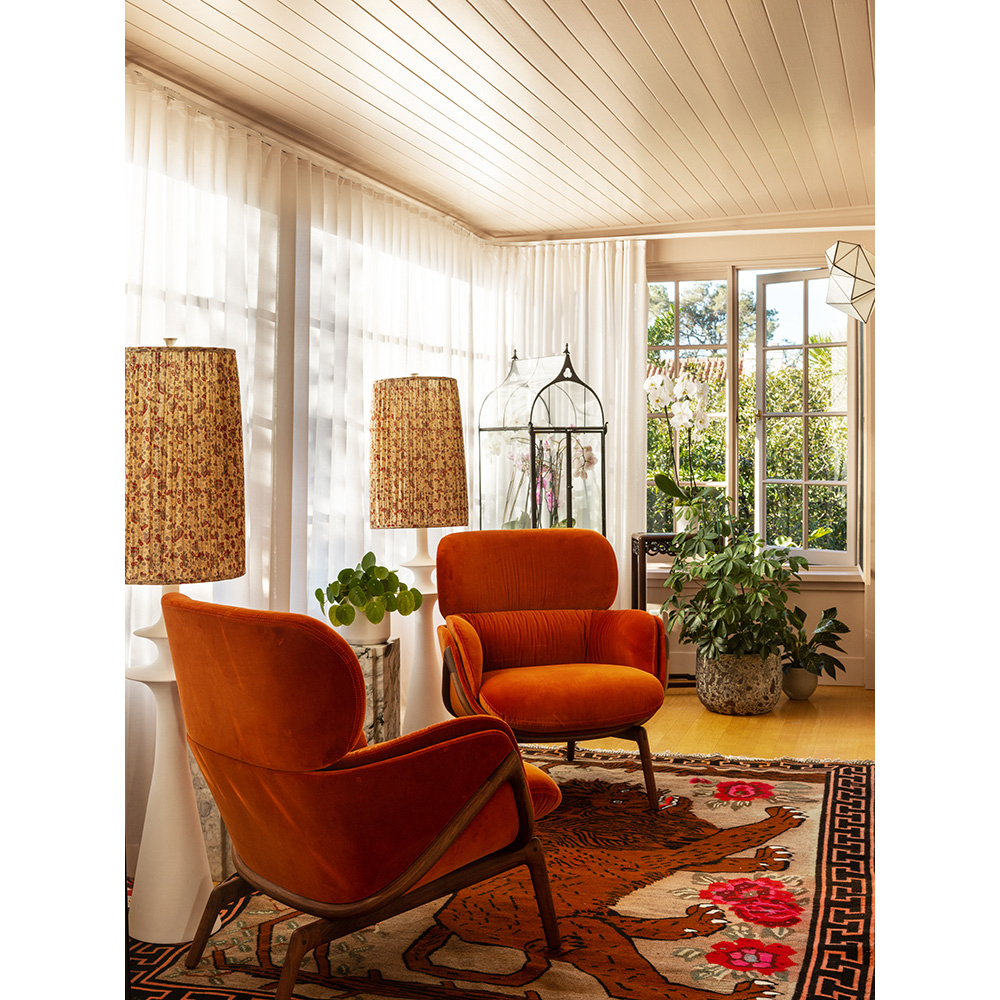 Living room interior with two orange armchairs, patterned lamps, plants, and a patterned rug with a geometric border and a bear design.