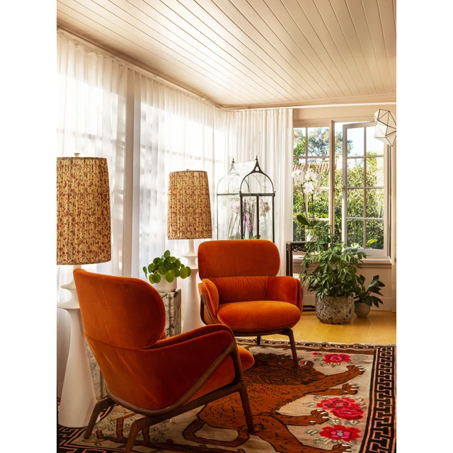 Living room interior with two orange armchairs, patterned lamps, plants, and a patterned rug with a geometric border and a bear design.