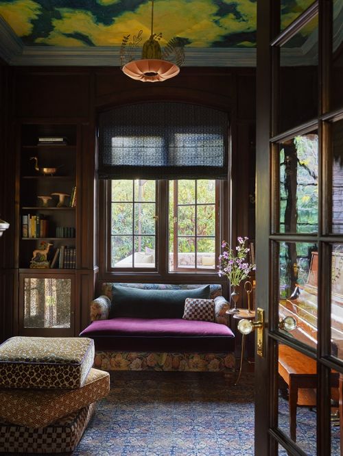 Living room interior with a window and view, featuring a cushioned bench, patterned rug, and artful ceiling. Home decor and design.