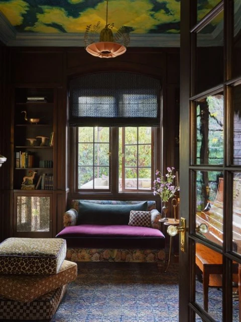 Living room interior with a window and view, featuring a cushioned bench, patterned rug, and artful ceiling. Home decor and design.