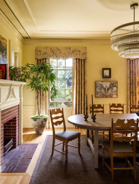 Interior view of a dining room with light yellow walls, a round table with chairs, and a fireplace with a green potted plant.