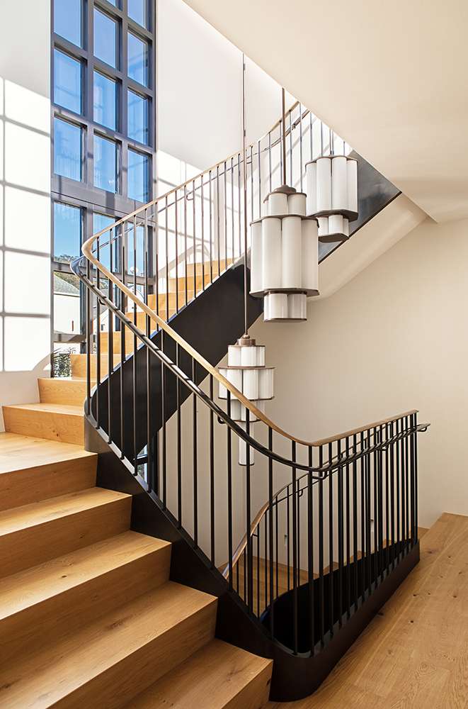 Interior view of a modern staircase featuring wooden steps, a black metal railing, and hanging pendant lights in a well-lit setting.