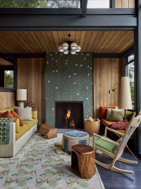 Cozy living room interior with a fireplace, wooden walls, a patterned rug, and comfortable seating creates a warm, inviting space.