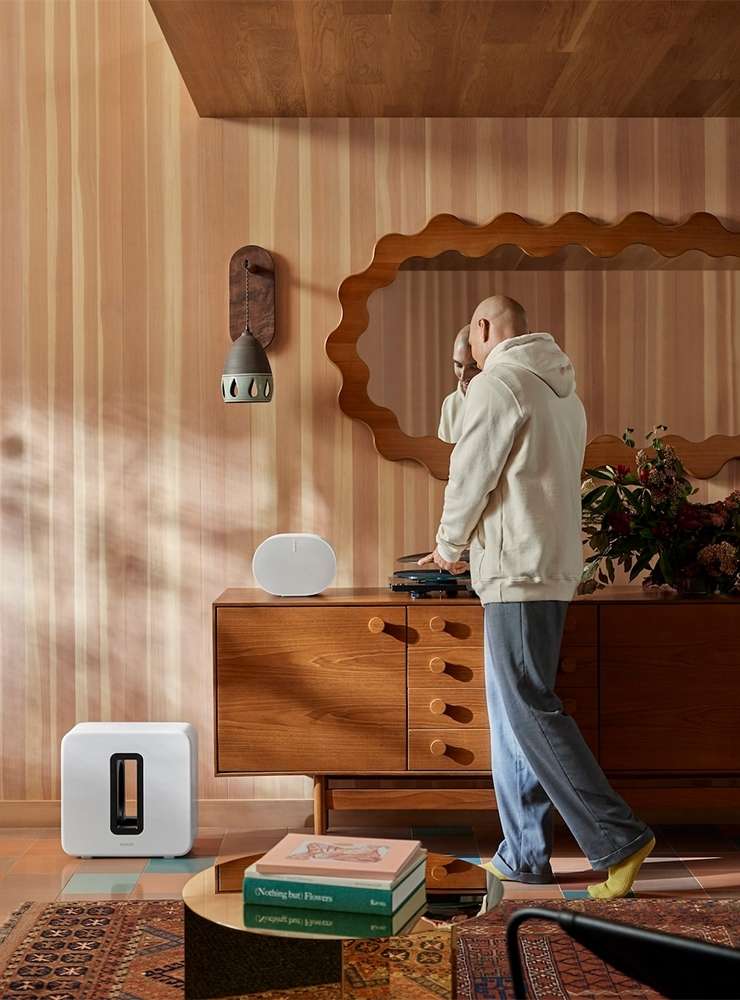 Interior shot of a modern living room featuring a man standing near a mid-century modern console table with speakers and decorative elements.