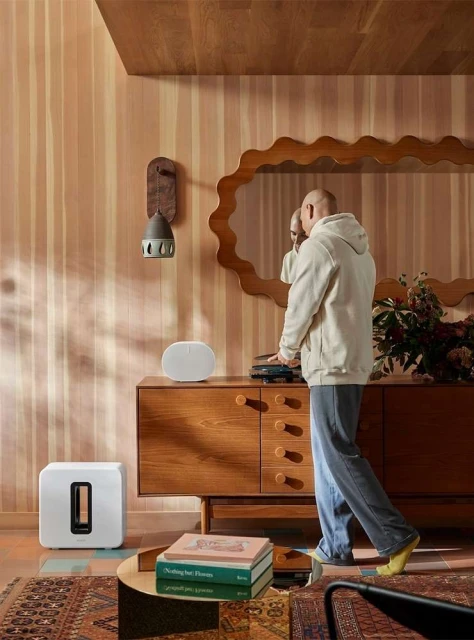 Interior shot of a modern living room featuring a man standing near a mid-century modern console table with speakers and decorative elements.
