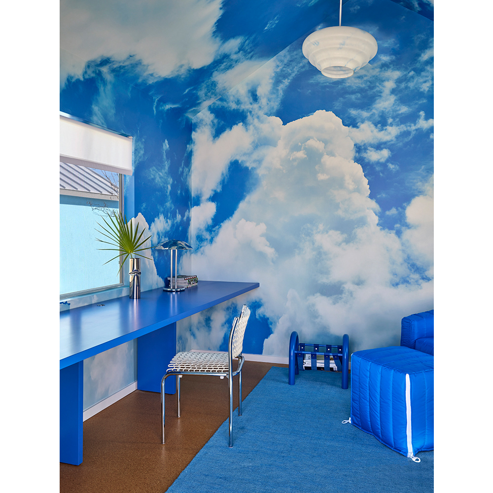 Interior space features a blue desk, chair, couch, and rug, with a cloud-patterned wall covering, creating a whimsical and modern design.