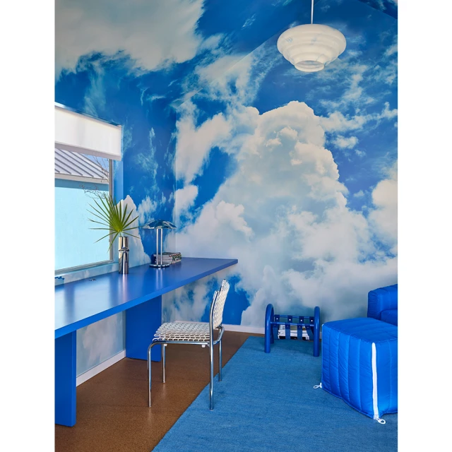 Interior space features a blue desk, chair, couch, and rug, with a cloud-patterned wall covering, creating a whimsical and modern design.