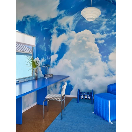 Interior space features a blue desk, chair, couch, and rug, with a cloud-patterned wall covering, creating a whimsical and modern design.