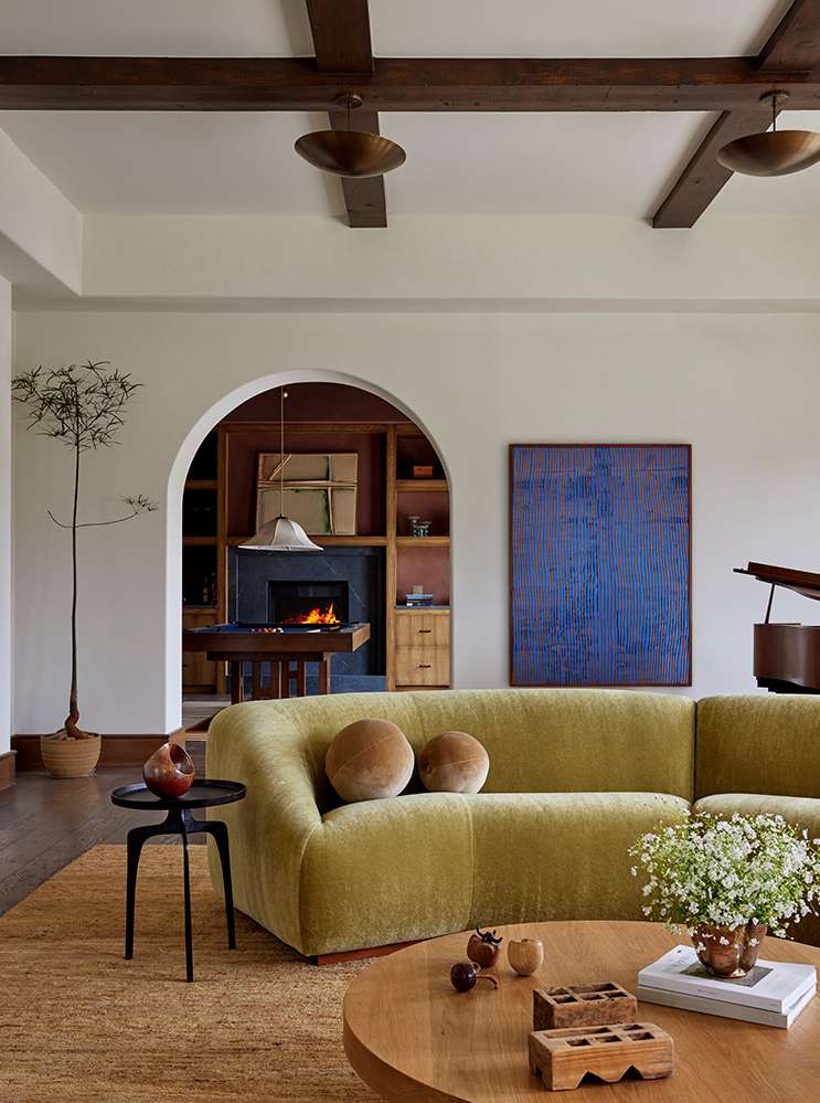 Living room interior featuring a green sofa, round wooden coffee table, a piano, and a fireplace with interior design elements.