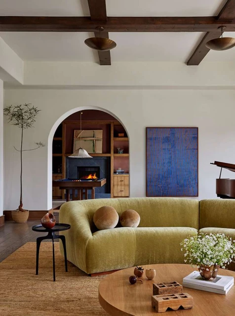 Living room interior featuring a green sofa, round wooden coffee table, a piano, and a fireplace with interior design elements.