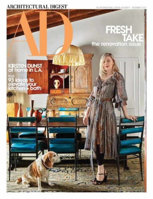 Architectural Digest cover featuring Kirsten Dunst, a beagle dog, blue dining chairs, and a vintage cabinet in a home interior setting.