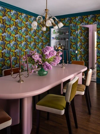 Interior dining room features a pink table centerpiece with lavender flowers, patterned wallpaper, and vintage-style chairs.