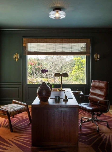 An interior view showcases a home office with a wooden desk, brown leather chair, a window view of greenery, and patterned rug.