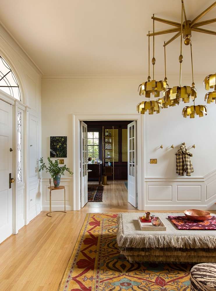 Luxurious home foyer with a patterned rug, unique chandelier, and white paneled walls, creating an inviting and stylish entrance.
