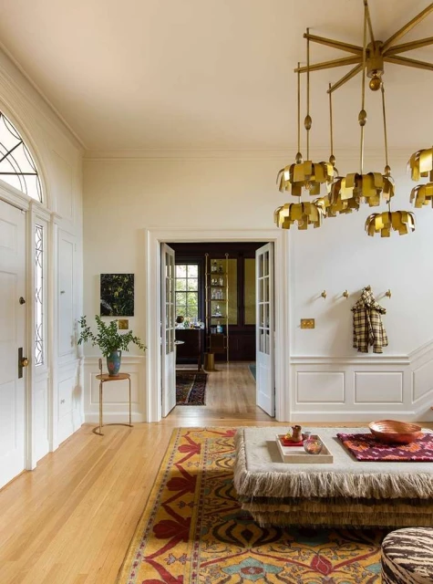 Luxurious home foyer with a patterned rug, unique chandelier, and white paneled walls, creating an inviting and stylish entrance.