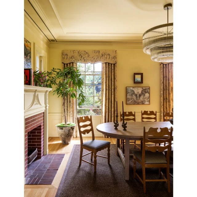 Formal dining room interior featuring a light wood table with chairs, a brick fireplace, and natural light from a window.