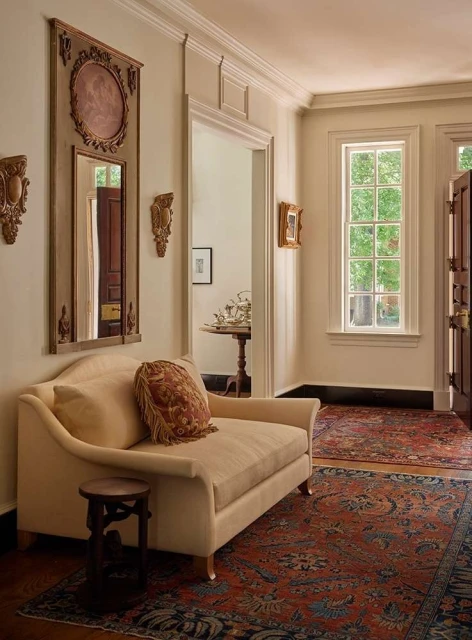Elegant interior hallway featuring a vintage settee, decorative wall mirror, patterned rug, and traditional architectural details.