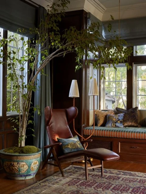 Living room interior featuring a wingback chair, floor lamps, and potted plant by the window, creating a cozy and inviting atmosphere.