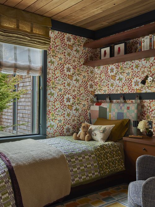 Cozy bedroom interior featuring a single bed with patchwork quilt, a teddy bear, floral wallpaper, and wooden ceiling.