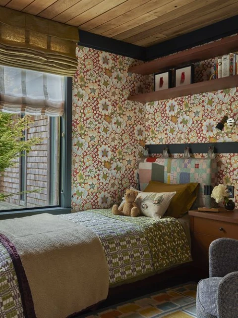 Cozy bedroom interior featuring a single bed with patchwork quilt, a teddy bear, floral wallpaper, and wooden ceiling.