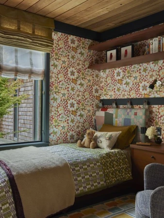 Cozy bedroom interior featuring a single bed with patchwork quilt, a teddy bear, floral wallpaper, and wooden ceiling.