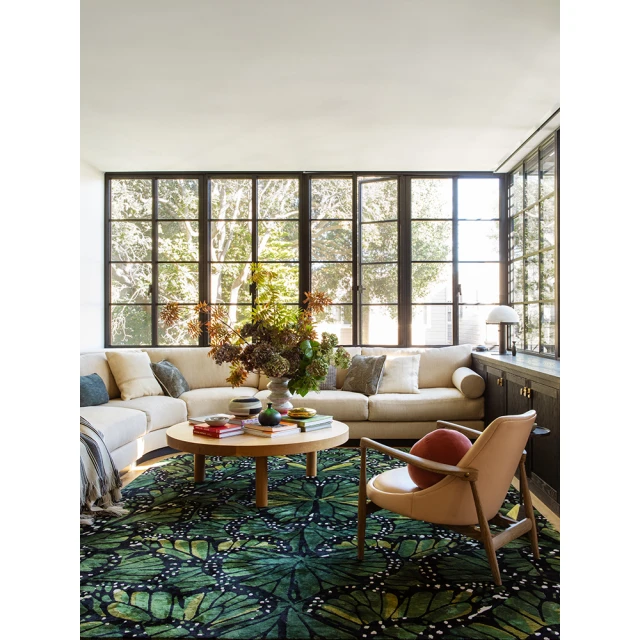Living room interior with a beige sectional sofa, round wood coffee table, and an armchair, complemented by a green butterfly-patterned rug.