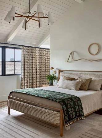 Bedroom interior with a platform bed dressed in neutral linens, a green patterned coverlet, and decorative wall hangings above the headboard.