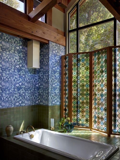 Bathroom interior featuring a white bathtub, blue floral wallpaper, green tiled accents, and a decorative circular-patterned screen.