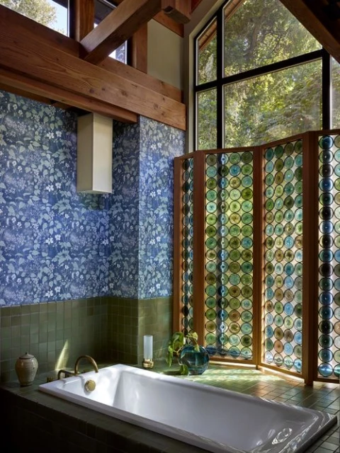 Bathroom interior featuring a white bathtub, blue floral wallpaper, green tiled accents, and a decorative circular-patterned screen.