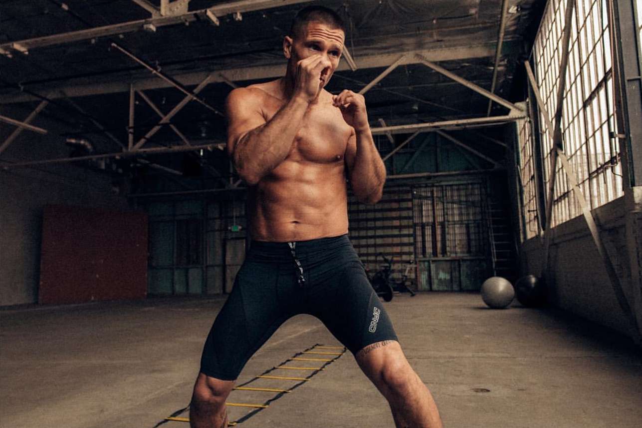 Muscular man in workout attire standing in an industrial-style space, hands up in boxing pose, ready to workout. Fitness and sports.